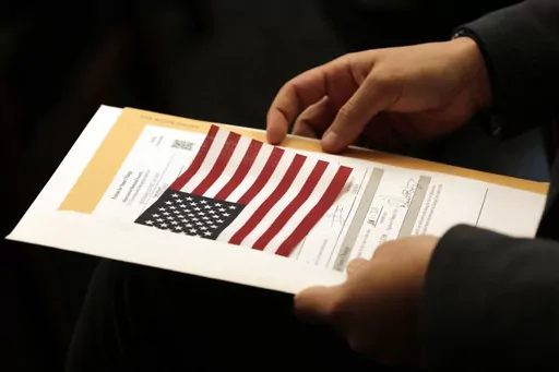 Abdullah Omar, from Iraq, holds his information packet and an American flag during a naturalization ceremony on Jan. 17, 2020, in Cleveland. Two decades after the U.S. invasion of Iraq, thousands of Iraqis are still trying to emigrate to the United States. An estimated 164,000 Iraqis have already found homes in America since the 2003 invasion. But many are still waiting. (AP Photo/Tony Dejak, File)