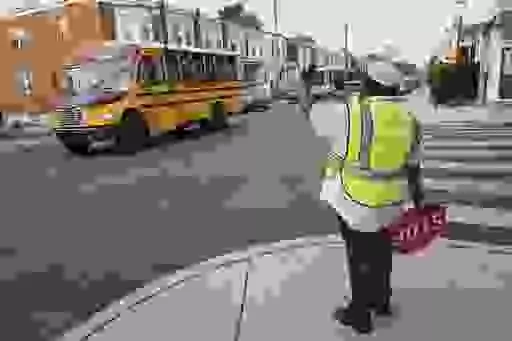 Crossing guard Pamela Lane waves a school bus passing her intersection, Master and N. 57th Street as she crosses students going to Bluford Elementary School, Tuesday, Sept. 5, 2023, in Philadelphia. Today is the first day of school of Philadelphia public school students on Tuesday. (Alejandro A. Alvarez/The Philadelphia Inquirer via AP)