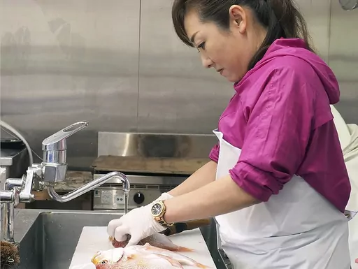 In this undated photo provided by Yoshie Minamidani, Minamidani cuts a fish at her seafood store in Wajima, Ishikawa prefecture, Japan. Minamidani is a survivor of a powerful earthquake that hit western Japan on New Year’s Day. The seafood store she ran in Wajima, the hardest hit city, was seriously damaged, as was the storage filled with her precious preserved fish. She told The Associated Press Tuesday she is determined to bring Wajima back. (Yoshie Minamidani via AP)