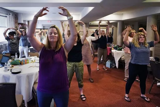CORRECTS INSTRUCTORS NAME TO EMILY DANIELS FROM EMILY RILEY Instructor Emily Daniels, left, raises her arms while leading a workshop helping teachers find a balance in their curriculum while coping with stress and burnout in the classroom, Tuesday, Aug. 2, 2022, in Concord, N.H. School districts around the country are starting to invest in programs aimed at address the mental health of teachers. Faced with a shortage of educators and widespread discontentment with the job, districts are hiring m