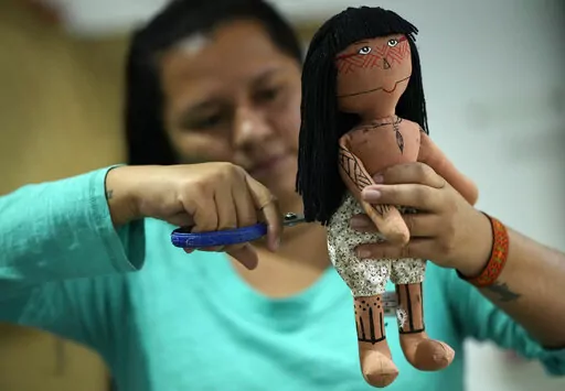 Atyna Pora, of Brazil's Anambe indigenous group, clips the hair made of yarn of an indigenous doll, at a sewing workshop in Rio de Janeiro, Brazil, Tuesday, May 24, 2022. Pora and her mother Luakam Anambe who make the dolls bearing faces and body paints of different Indigenous groups, have sold more than 5,000 of their dolls.  (AP Photo/Silvia Izquierdo)